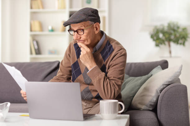 istock Elderly man sitting on a sofa at home and reading a paper document 1396439142