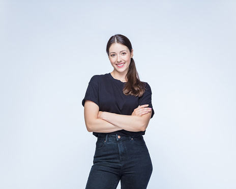 Portrait of happy young woman wearing black clothes standing with arms crossed against white background