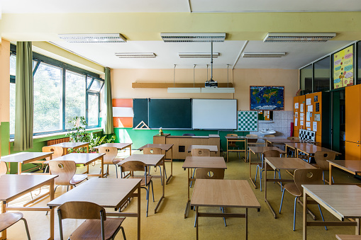 Interior of classroom in elementary school. Row of empty desks are in room.