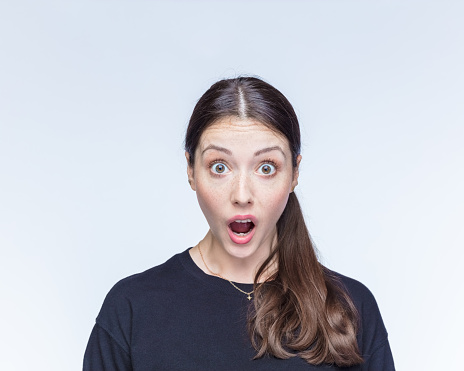 Portrait of young shocked woman with raised eyebrows against white background.