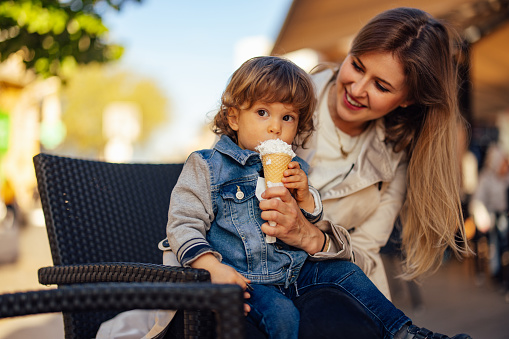 Toddler sitting with his mom, eating an ice cream, looking dirty.