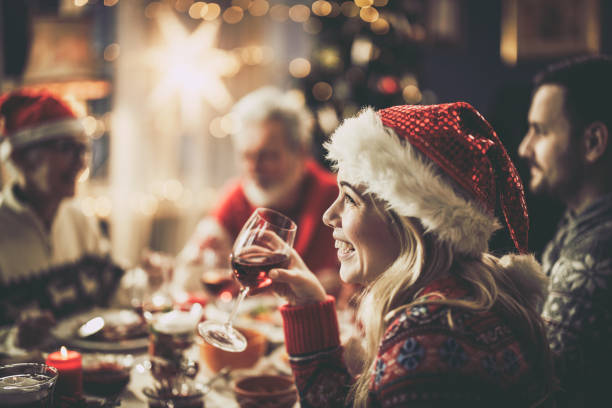 Happy woman with Santa's drinking wine during Christmas lunch at dining table. stock photo