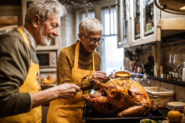 felice coppia senior che decora il tacchino il giorno del ringraziamento. - stuffed turkey foto e immagini stock