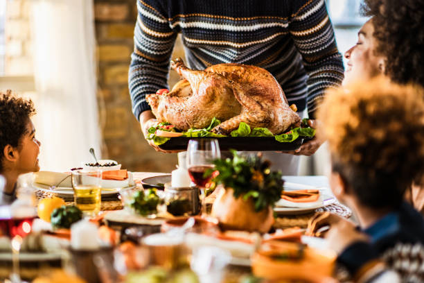 It is time for Thanksgiving turkey you all! Unrecognizable black father carrying Thanksgiving turkey while serving it for his family in dining room. thanksgiving turkey stock pictures, royalty-free photos & images