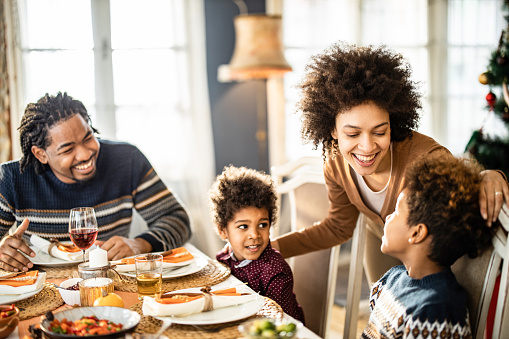 Happy black family communicating while having a meal in dining room.