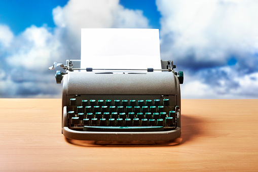 Typewriter on a desk with a summer sky in the background.
