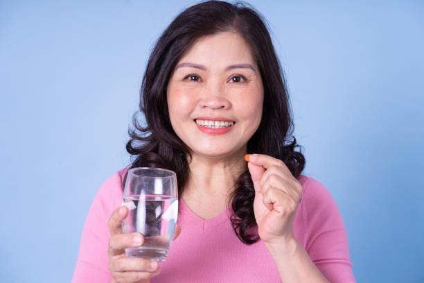 istock Image of middle aged Asian woman using pill on blue background 1396444478