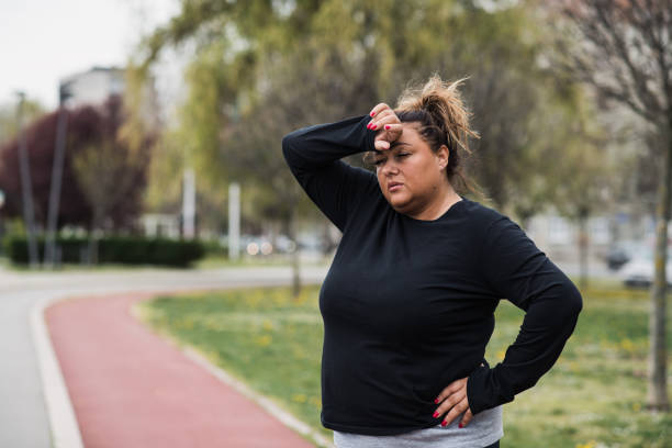 mujer obesa que se siente mareada en medio de ejercicios cardiovasculares - mature adult sadness overweight women fotografías e imágenes de stock