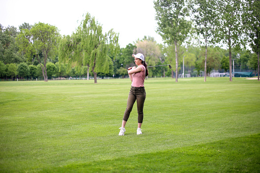 Female golf player on a golf course. About 25 years old, Caucasian brunette.