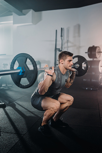 Determined young muscular male athlete exercising with barbell during weight training in gym
