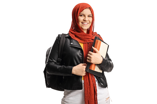 Young female student with a hijab holding books and looking at camera isolated on white background