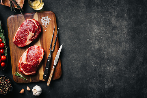 Raw beef steak with spices on cutting board. Dark stone background, top view scene with copy space