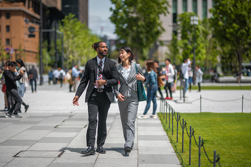 Full length front view of a black male lawyer and an asian female colleague working while walking through the city. They are discussing about the meeting at the office earlier in the morning.