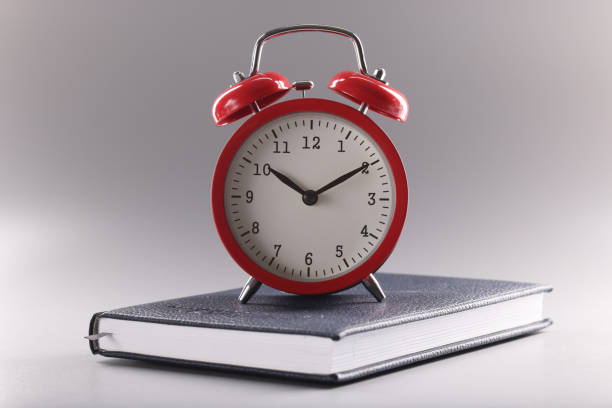 istock Red retro clock stand on top of closed book or diary, time to study, time to learn new information 1396458549
