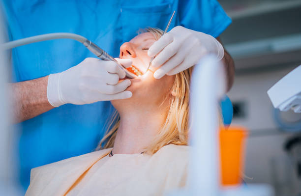 Female dentist extracting her male's patient teeth. The view is through glass.