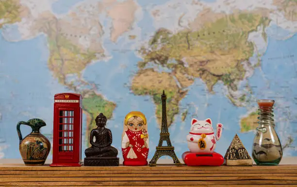 Souvenirs from around the world on the background of the world map. Greec amphora, London red booth, statue of Buddha, russian doll Matryoshka, Eiffel tower, Maneki neko, egiptian pyramid, arabian bottle with colour sand.