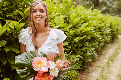 Young romantic bride during wedding, standing at vegetation wall with a bouquet of flowers, on the beautiful countryside way. Love, relationships, romance, happiness concept.