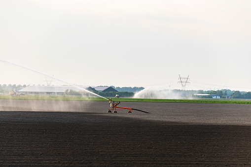 Irrigation pivot gun machine spraying water on a field during a dry and warm spring day in Flevoland, Netherlands. Over the last years there have been longer periods of draught causing problems for farmers cultivating crops.