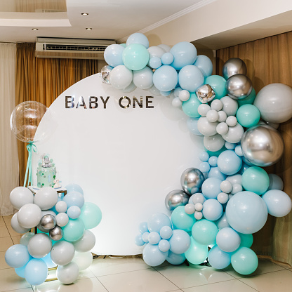 Arch decorated with blue, green, grey, and silver balloons. Baby one party. Trendy Cake for 1 year. Birthday Cake on a background photo wall. Delicious reception at a birthday party.
