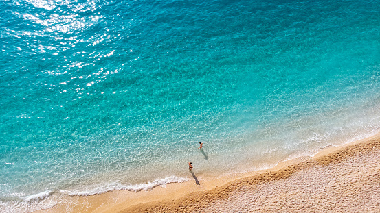 Vista aérea de la pareja de pie en una hermosa playa de arena con suave ola turquesa del océano. Mar tropical en temporada de verano en la playa de Porto Katsiki en la isla de Lefkada. photo