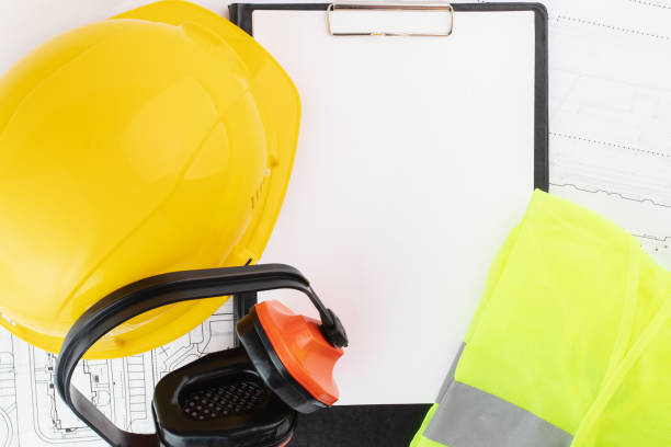 istock protective vest, engineer's helmet, earmuffs, clipboard text mockup on background of architectural drawings 1396463882