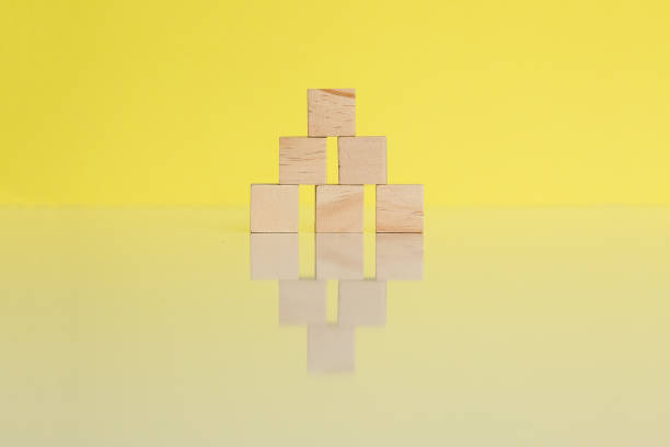 istock Wooden cubes arranged together in triangular pyramid, mirrored on yellow background. Conceptual and symbolic image. Copy space. 1396466159