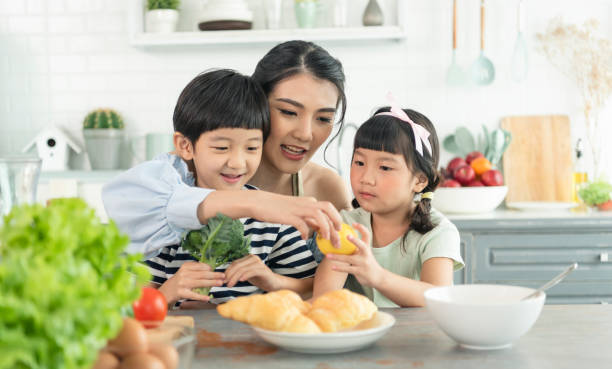 Asian young single mother with son and daughter in kitchen. Enjoy family activity together. stock photo