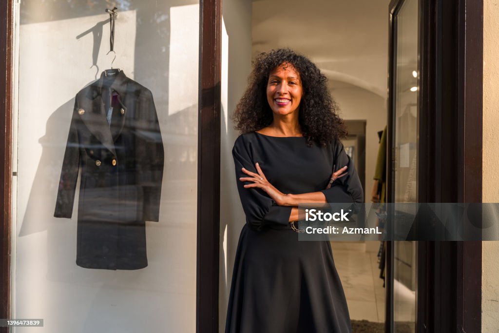 Haute Couture in Hands of Female Management A 3/4 length shot of a mid adult female fashion shop owner, standing in front of the shop entrance with her arms crossed and looking at the camera with a big, confident smile. Black Color Stock Photo