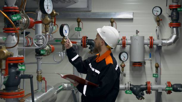 A bearded man with blue eyes in overalls and a helmet. The engineer checks the pressure readings in the pipeline using pressure gauges and compares them with the allowable pressure settings. A bearded man with blue eyes in overalls and a helmet. The engineer checks the pressure readings in the pipeline using pressure gauges and compares them with the allowable pressure settings. wellhead stock pictures, royalty-free photos & images