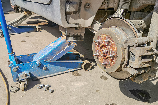 Jacking up a car to change a tire. Replacing car wheel using hydraulic jack. Car without wheel lift up by hydraulic, waiting for tire replacement. Brake discs without wheels.