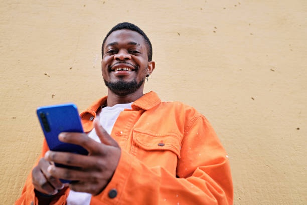 istock View from below of a young man using his cell phone against a wall looking at the camera. 1396476894