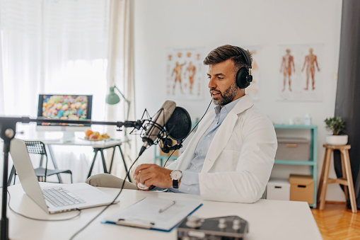 One young doctor hosting a medical podcast. He is talking to a microphone and broadcasting on internet
