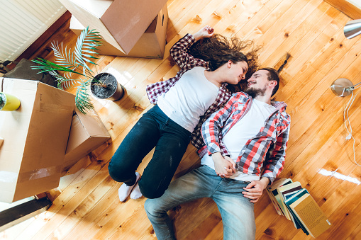 Excited cute Caucasian couple moving to new apartment. Lying on floor surrounded with boxes.
