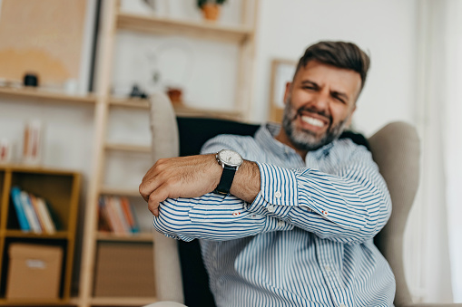 Young mid adult man sitting in the living room and having a elbow pain