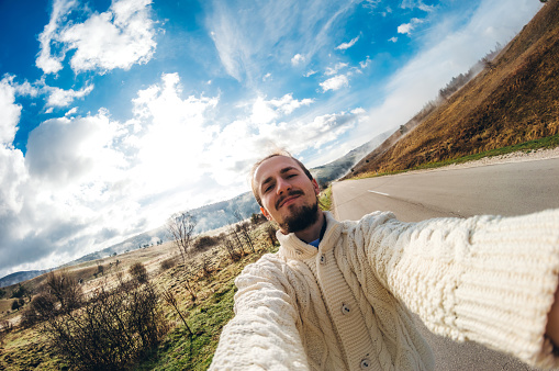 Summer holidays and people concept - happy smiling young man in sweater taking selfie on road.