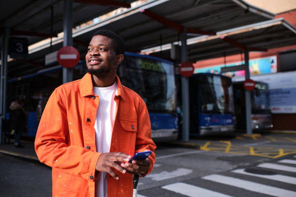 istock A young man waiting at a bus terminal holding his cell phone while looking to see if his bus is coming 1396479297