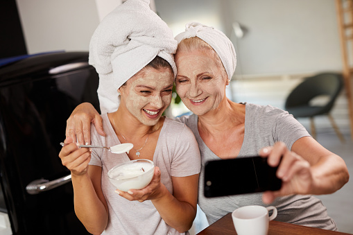 Smiling women with facial masks on talking selfie at home