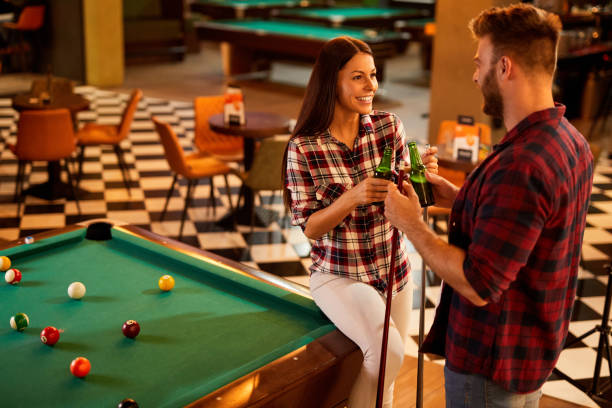 Young couple playing pool and drinking beer on a date in pool hall stock photo