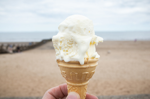 Close-up of a vanilla ice cream in a cornet / cone, at the beach on a cloudy day. Portobello beach, Edinburgh, Scotland.