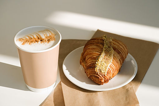 Coffee to go in a paper cup with croissants on table. Takeaway breakfast