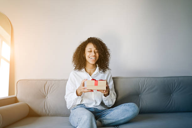 istock Excited african American young woman sit on couch at home unpack gift box 1396483473
