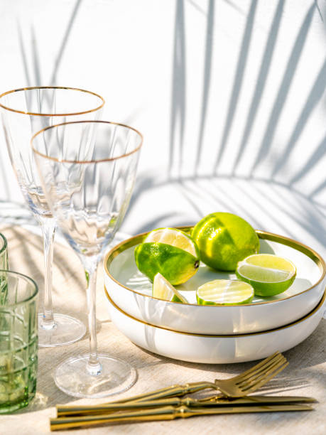 istock Preparing beverages for summer tropical event. Setting for day time party with tableware, wine glasses. Background with hard light and palm leaves shadows. 1396484519