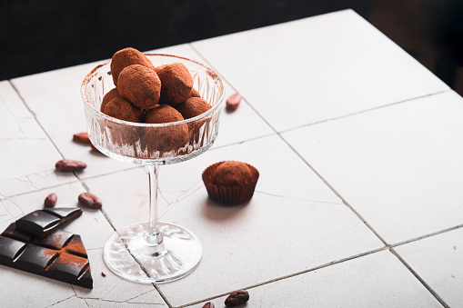 Chocolate truffles. Homemade chocolate truffles with cocoa powder on glass on old cracked tile table background. Tasty sweet chocolate truffles candies. Valentine's Day and Mother's Day concept.