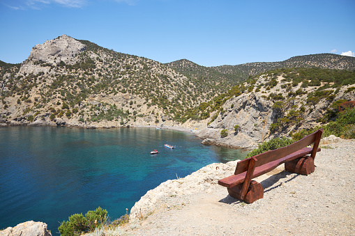 Wooden bench on a rock with a view of a beautiful bay with transparent water in the summer