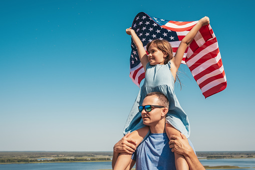 Happy family father and child with USA flag enjoy nature. The concept of freedom, lifestyle.