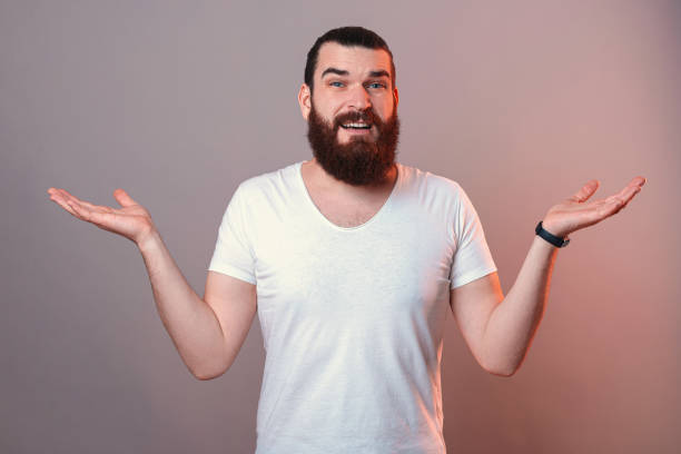 istock Young bearded man is shrugging over grey background in a studio. 1396490796