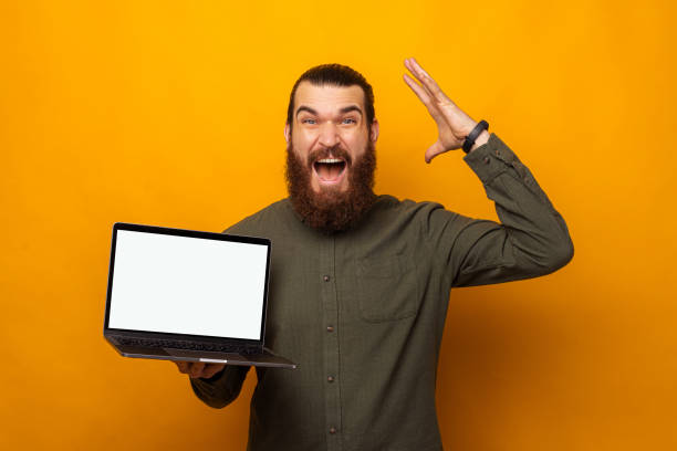 Ecstatic bearded man holding a laptop with blank screen is mind blown. stock photo