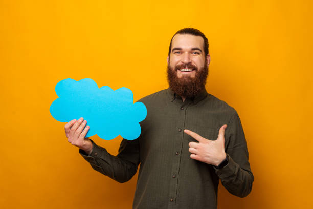 Happy bearded man is pointing at the blue cloud shaped speech bubble. stock photo