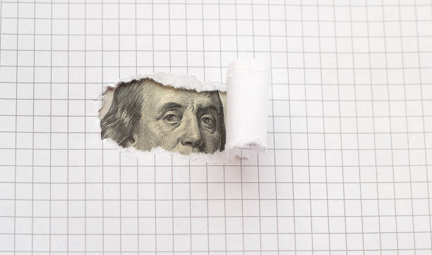 istock Benjamin Franklin peers through torn white paper. Concept. 1396493156