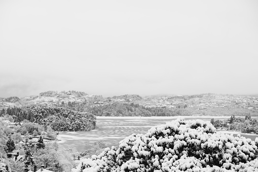 Early morning winter landscape at a fjord (Nordasvannet) near the City of Bergen on the west coast of Norway after snowfall. The seawater of the fjord is partly frozen and covered with snow. The image was captured on an overcast and cloudy day.